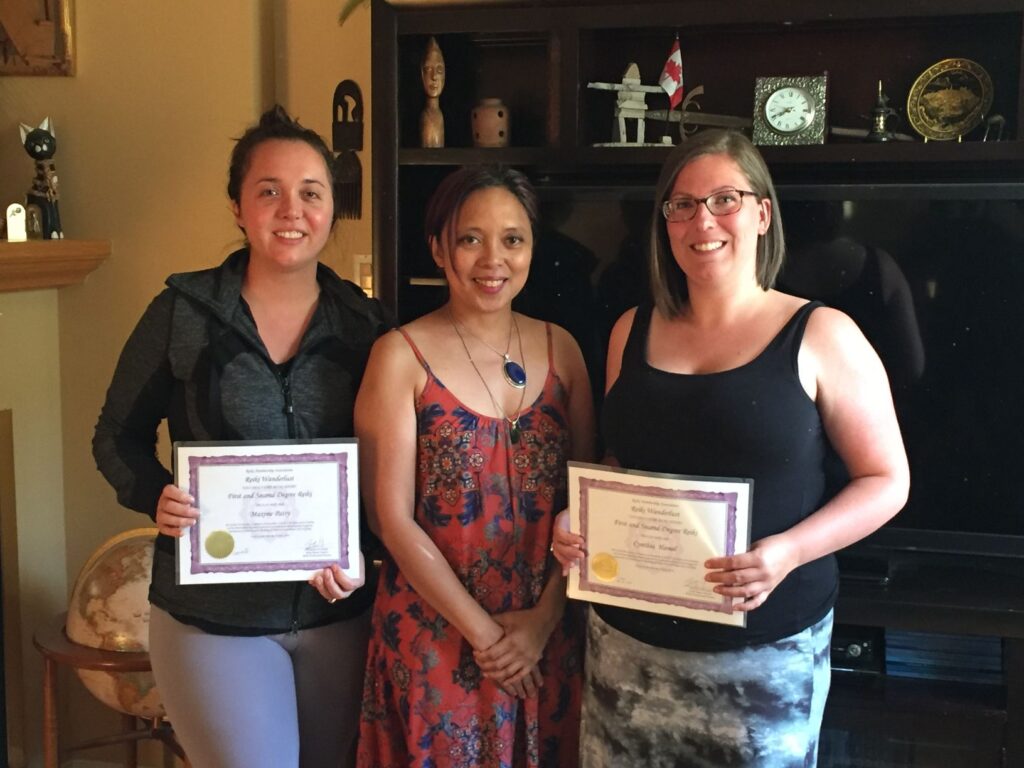 Three women holding certificates in front of a living room.