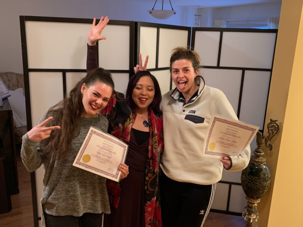 Three women holding certificates in front of a room.
