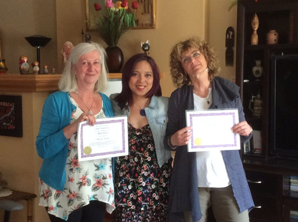 Three women holding certificates in front of a living room.